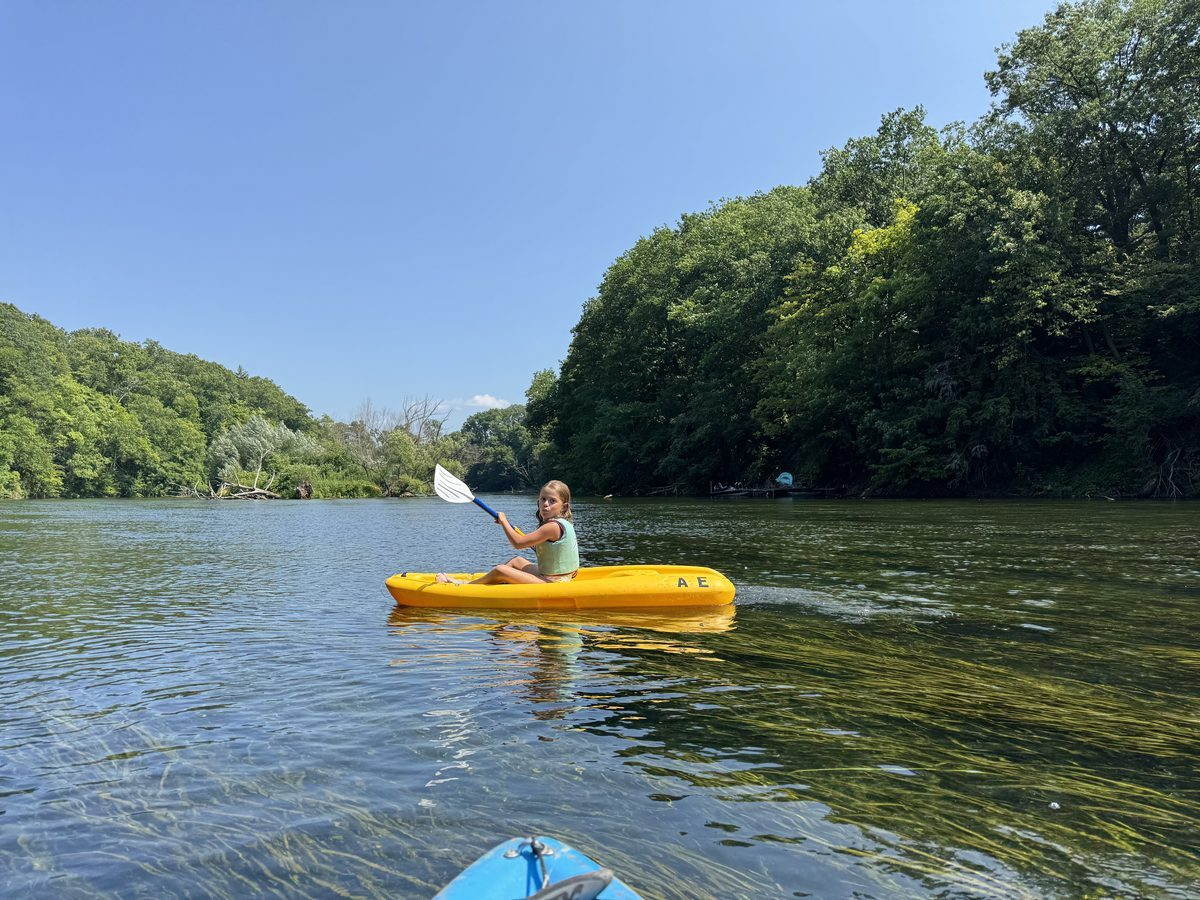 Girl paddling a yellow kayak on the Oak Orchard River lined with lush green trees